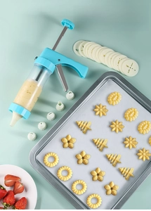 Close-up of a blue piping gun set with nozzles, flower discs, and fresh cookies