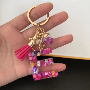 Detail of pink resin letter E keychain with gold ring, tassel, and sequin star glass ball