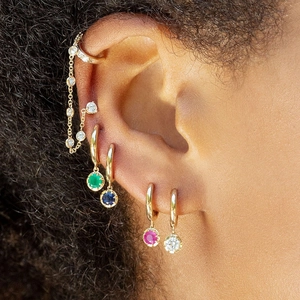 Detailed view of model wearing gold hoop earrings with multi-colored zircon gemstones