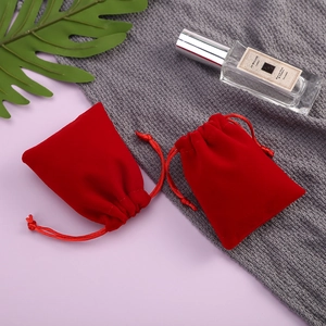 Detail of red velvet jewelry pouch with matching drawstring on a soft grey fabric backdrop