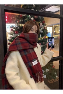 Close-up of a red and green plaid scarf with fringe and a white label in a cafe setting