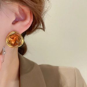 Close-up of geometric irregular amber resin stud earrings with a wide gold metal frame