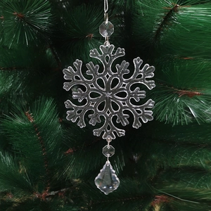 Close-up of clear acrylic snowflake pendant hanging on a green Christmas tree branch