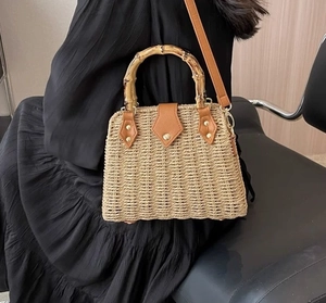 Detail of straw woven handbag with bamboo handle shown against a black dress