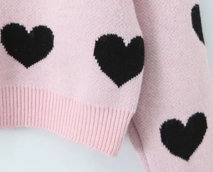 Detailed close-up of pink knit sweater with black heart patterns and ribbed hem detail
