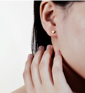 Detail of a small golden heart-shaped s925 silver stud earring worn on the earlobe