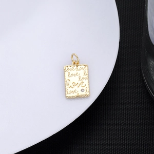 Macro view of gold pendant with engraved love text and a small zircon on edge