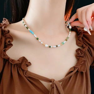Detail of elegant pearl necklace with green and blue gemstones on a female model