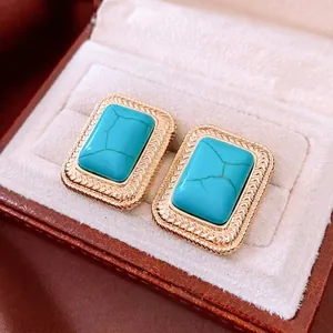Vintage gold square earrings with turquoise stones and wheat pattern texture on a display