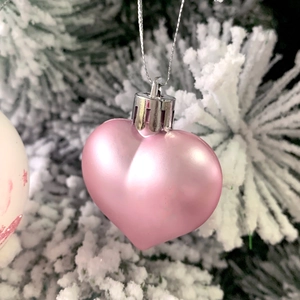 Close-up of a pink heart-shaped Christmas ornament hanging on a snowy pine branch