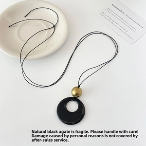 Detailed view of faux agate round pendant necklace with gold bead on a white plate