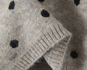 Dettaglio ravvicinato del maglione beige in maglia a pois neri con polsini a costine