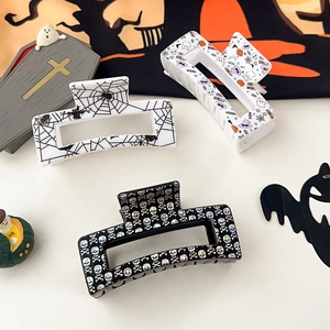 Three Halloween claw clips with spider web, ghost, and skull patterns on a flat surface