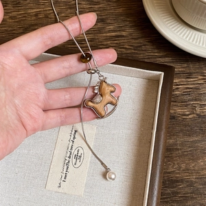 Detail of wooden horse pendant necklace featuring crystal saddle and elegant pearl drop
