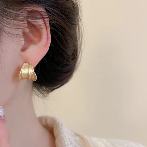 Close-up of golden wavy brushed metal stud earrings worn on model for a minimalist look