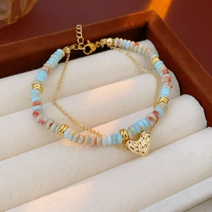 Macro view of double-layered beaded bracelet with gold heart pendant and lobster clasp