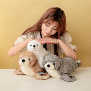 Tre teneri peluche a forma di foca in bianco, marrone e grigio con modella donna