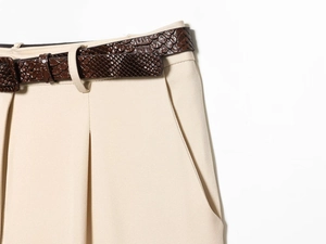 Gros plan d'un short beige avec ceinture en peau de serpent et détail de la poche latérale