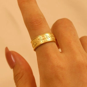 Macro shot of wide gold stainless steel ring with eye pattern embossing on finger