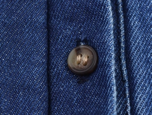 Nahaufnahme von dunkelblauem Denim-Stoff mit braunem Knopf und präziser Nahtverarbeitung