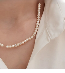 Close-up of natural cream white pearl necklace styled with a white stand-collar shirt