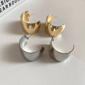 Macro detail of polished gold and silver C-shape wide hoop earrings on a neutral background