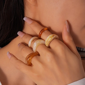 Fashionable resin acrylic rings with marble texture and amber tones worn by model