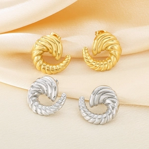 Detailed macro view of gold and silver irregular spiral croissant stud earrings on silk cloth