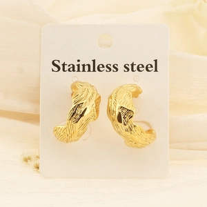Détail macro de boucles d'oreilles C dorées en acier avec une texture plissée unique