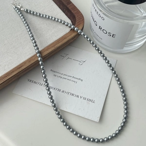 Elegant gray faux pearl necklace displayed next to a premium perfume bottle and wooden tray