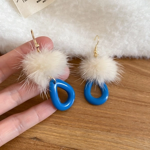 Detail view of blue resin teardrop earrings with fuzzy pompom and gold metal hooks