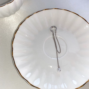 Detailed view of silver tassel ear cuff with a pearl drop on a white porcelain dish