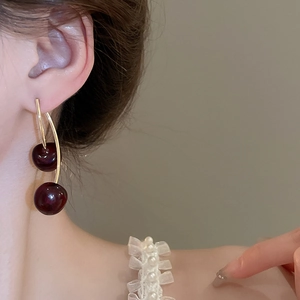 Close-up of elegant dark red cherry earrings with gold curved stems on a model