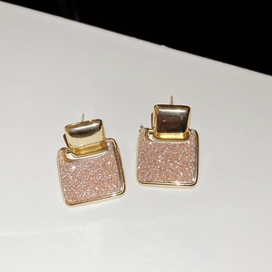 Close-up of 18k gold plated square drop earrings with sparkling pink glitter inlay