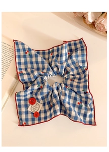 Detailed close-up of blue plaid scrunchie with red cherry embroidery and button accents