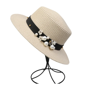 Detail of summer straw hat featuring black ribbon with pearls and 3D floral accents