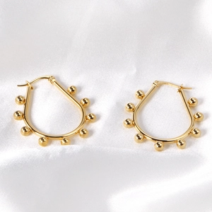 Macro shot of gold teardrop earrings with bead accents on white satin background