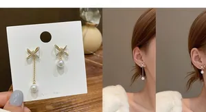Detail of asymmetric bow pearl earrings featuring gold tassel and zircon accents
