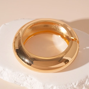 Detail of wide gold chunky hinge bangle with mirror finish on natural stone