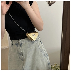Détail du sac bandoulière triangulaire doré avec boucle papillon et bandoulière chaîne