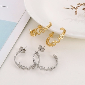 Detail of gold and silver C-shaped Love letter hoop earrings on a decorative plate