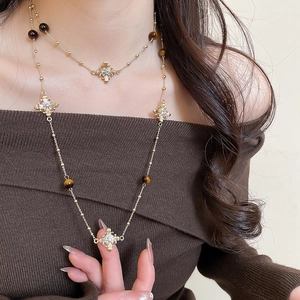 Detail of layered gold cross necklace with tiger eye beads on a fashion model