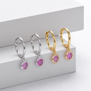 Detailed view of round pink gemstones hanging on silver and gold earring hoops