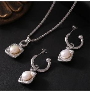 Detailed close-up of a vintage silver necklace and matching pearl earrings on black background