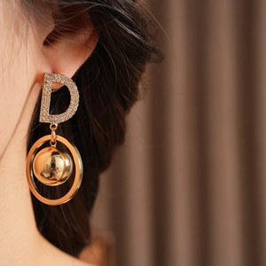 Close-up of golden letter D earring with pavé rhinestones and a spherical ball pendant