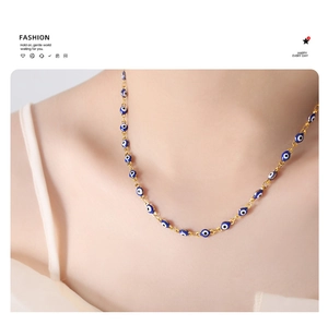 Detail of gold-plated chain necklace with blue and white evil eye enamel beads on neck