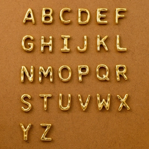 Flat lay of 26 gold bubble-style stainless steel A-Z alphabet charms on brown background