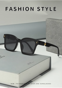 Detail view of black oversized sunglasses with gold metal accents on modern grey background