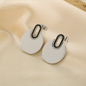 Detailed close-up of polished silver hoop earrings with black hollow design on gold satin