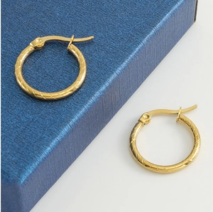 Macro detail of gold textured 18k stainless steel hoop earrings on blue gift box background